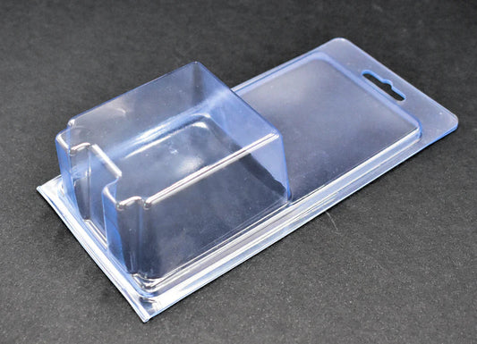 A clear rectangular blister package with a hanging tab, designed for small products, placed on a black surface.